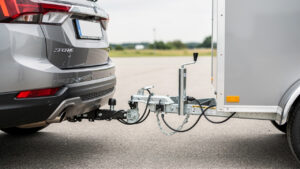 Vue arrière réaliste d’un véhicule muni d’un attelage col de cygne relié à une petite remorque bagagère, avec le raccordement électrique visible sous une lumière naturelle.
